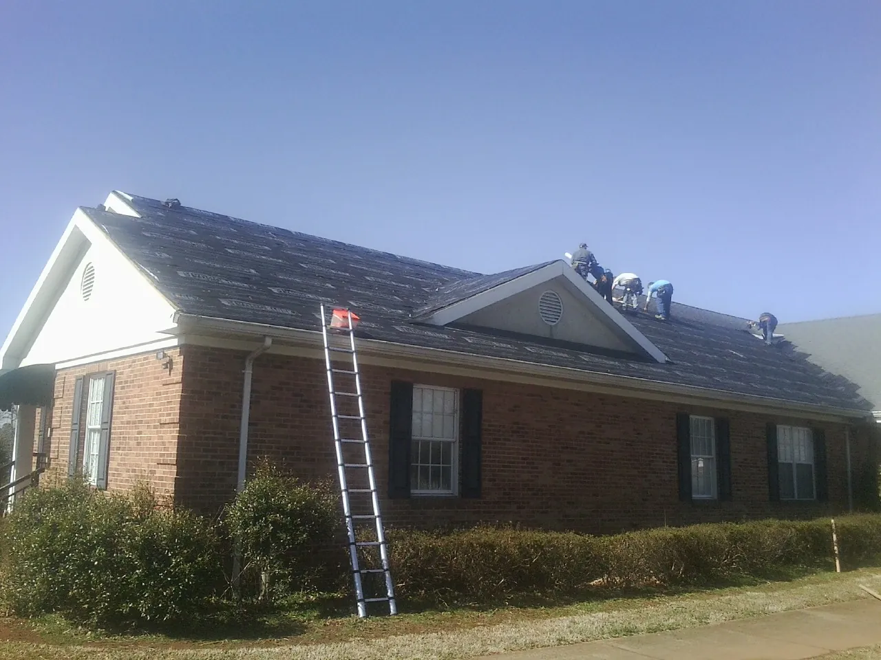 Crew tearing shingles off a brick ranch roof with a ladder set — Emergency Roof Repair work by our crew in Cross River