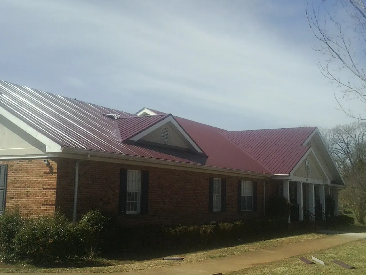 Red metal roof with gabled entries on a long brick building, from a Hail Damage Roof Repair job in Cross River