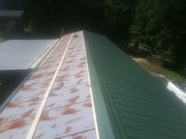 Old rusted panels beside newly installed green metal roofing — Wind Damage Roof Repair by Roofing Brothers in Cross River