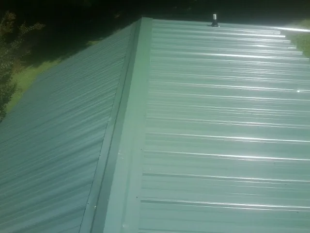 New green metal panels meeting at the ridge of a roof — Flat Roof Repair work by our crew in Cross River