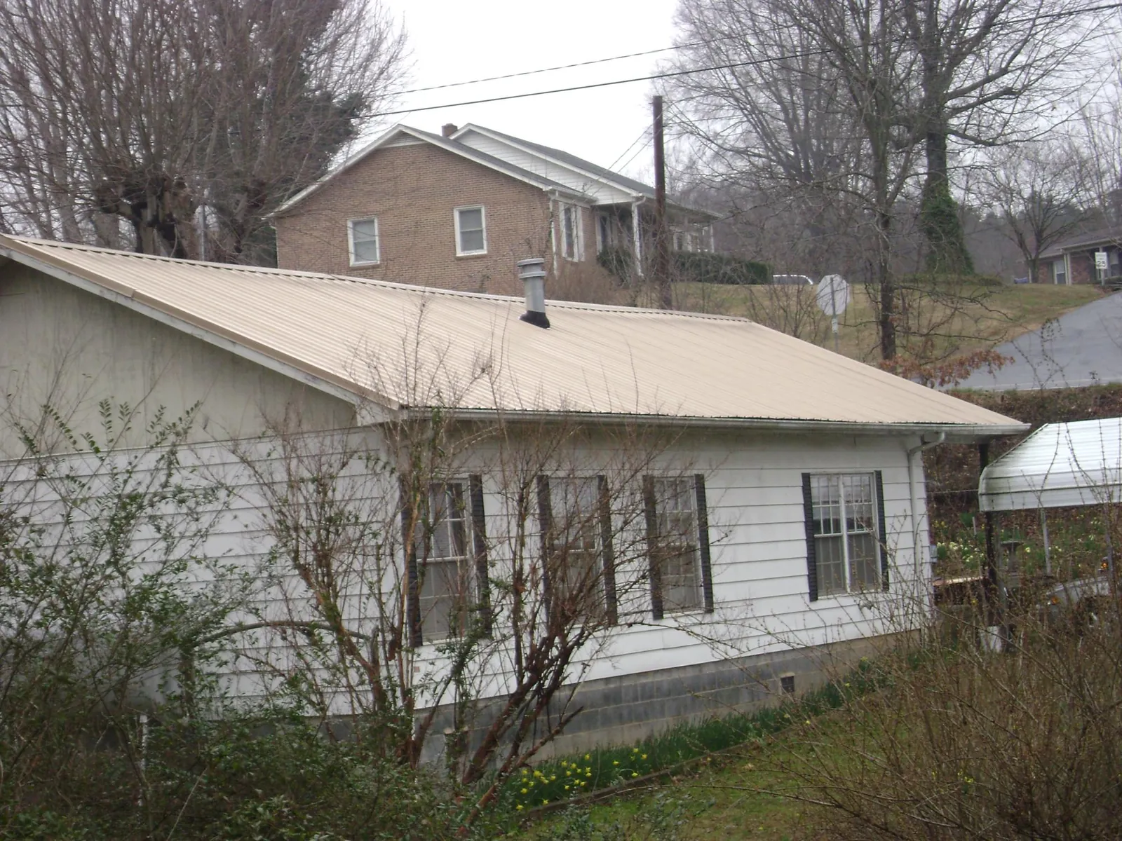 Tan metal roof on a white sided house set into a hillside — Commercial Roofing by Roofing Brothers in Cross River